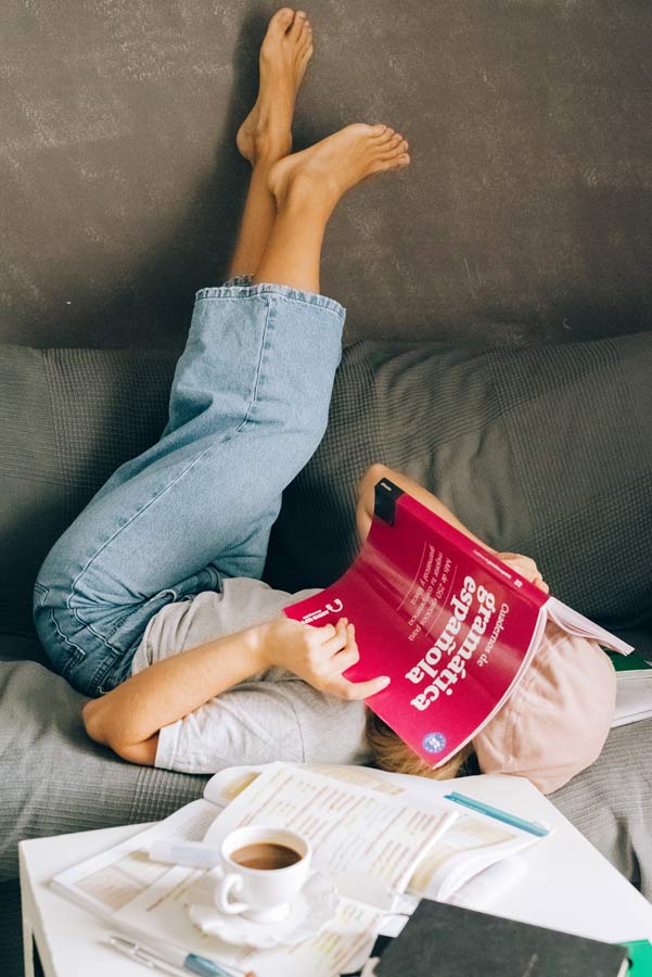 Girl learning Spanish with a grammar book in a sofa